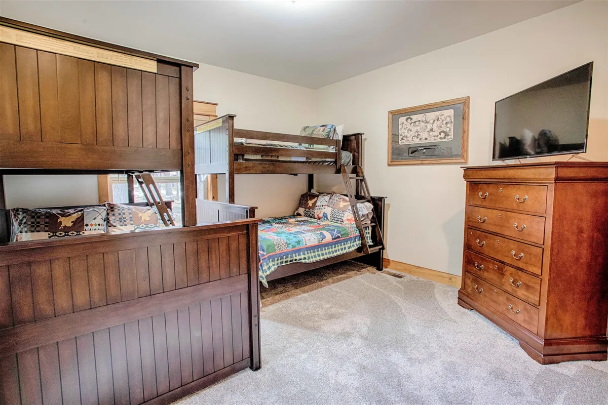A cheerful bunk room with a sturdy wooden bunk bed, dresser, wall art, and a television, designed to be inviting for younger guests. The space is playful yet cozy, perfect for kids to unwind, play, or watch movies together.