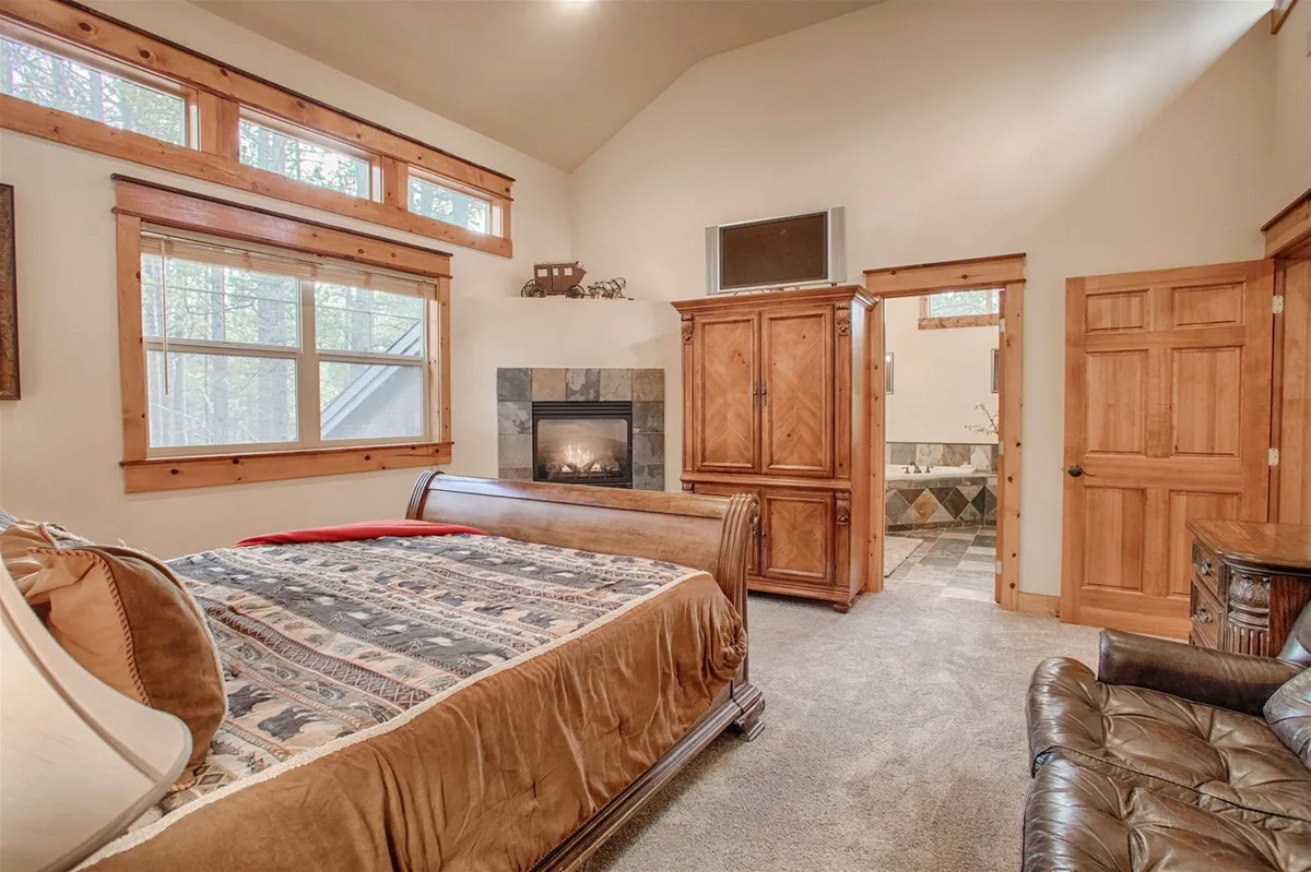 A spacious bedroom featuring a king sleigh bed, cozy fireplace, wooden furniture, and large windows letting in natural light. The room feels luxurious and serene, perfect for rest and relaxation after a long day.