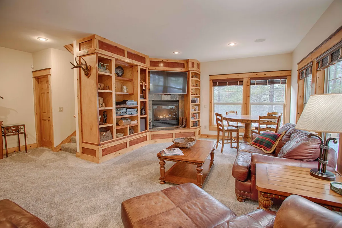 A warm, inviting living space with a cozy fireplace, wall-mounted bookshelves, and a comfortable leather sofa. The room is set up for family gatherings, with sightlines to a dining table and entertainment area, suggesting evenings spent watching movies or playing games by the fire.
