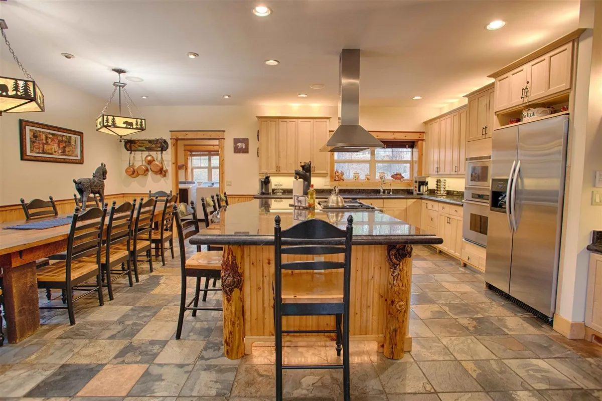 A spacious chef's kitchen with a large central island, modern stainless steel appliances, and decorative lighting. The kitchen opens toward a dining area, making it ideal for shared meal preparation and entertaining guests.