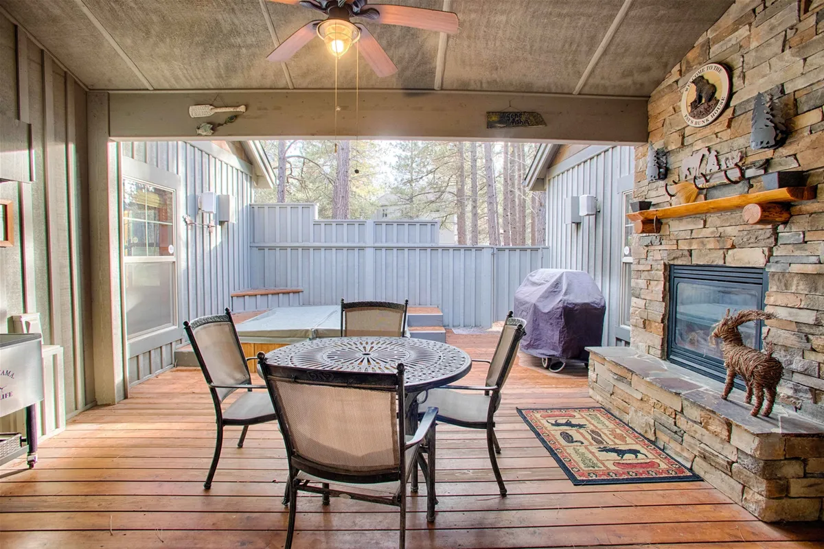 A circular dining table positioned near a stone fireplace, opening directly onto a wooden deck. The area is warm and inviting, ideal for intimate gatherings or sunset dinners, blending indoor and outdoor living seamlessly.
