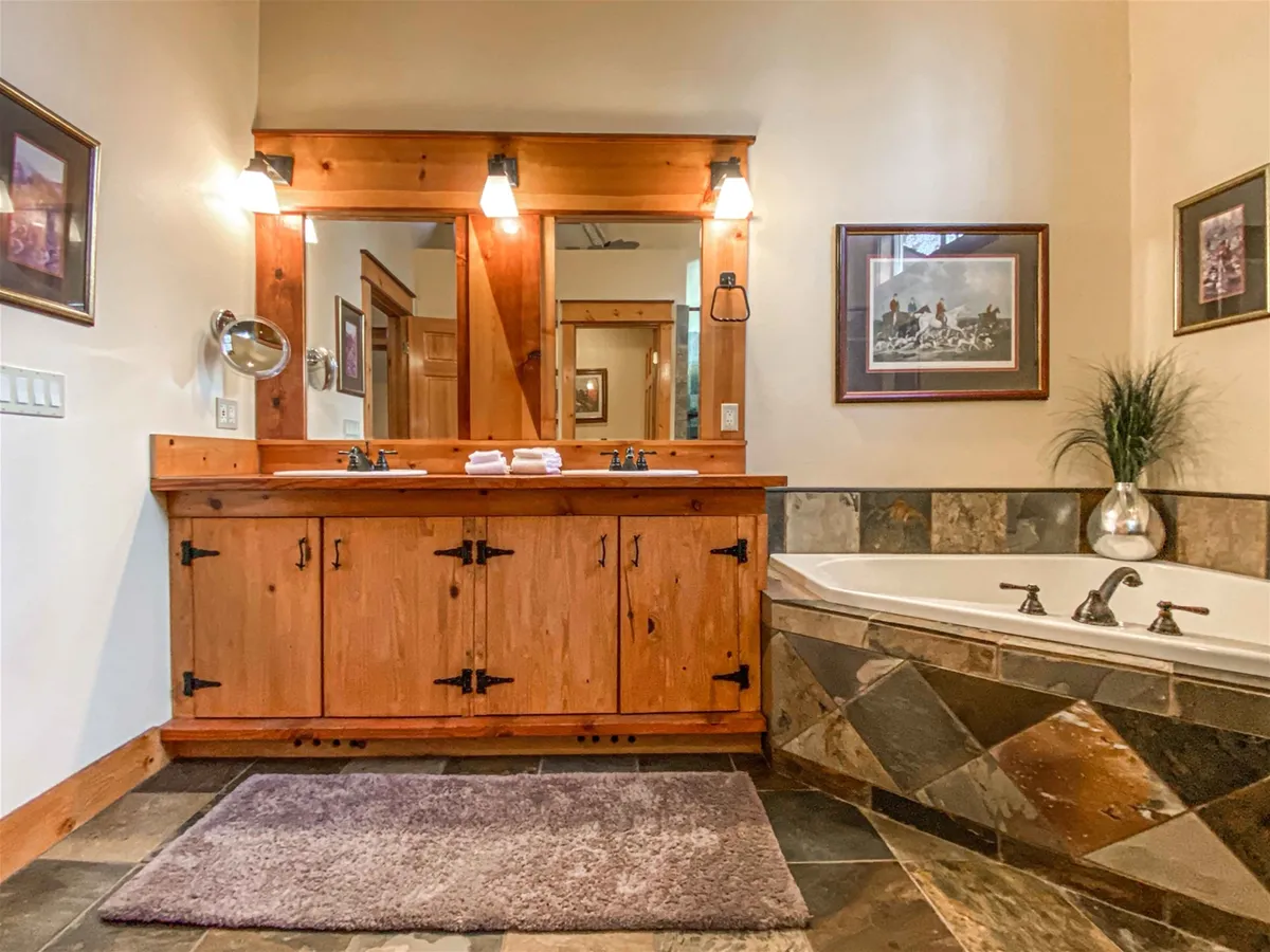 A luxurious bathroom with a double sink vanity, freestanding soaking tub, decorative mirrors, and elegant artwork. The space feels tranquil, offering a spa-like atmosphere for relaxation and self-care routines.