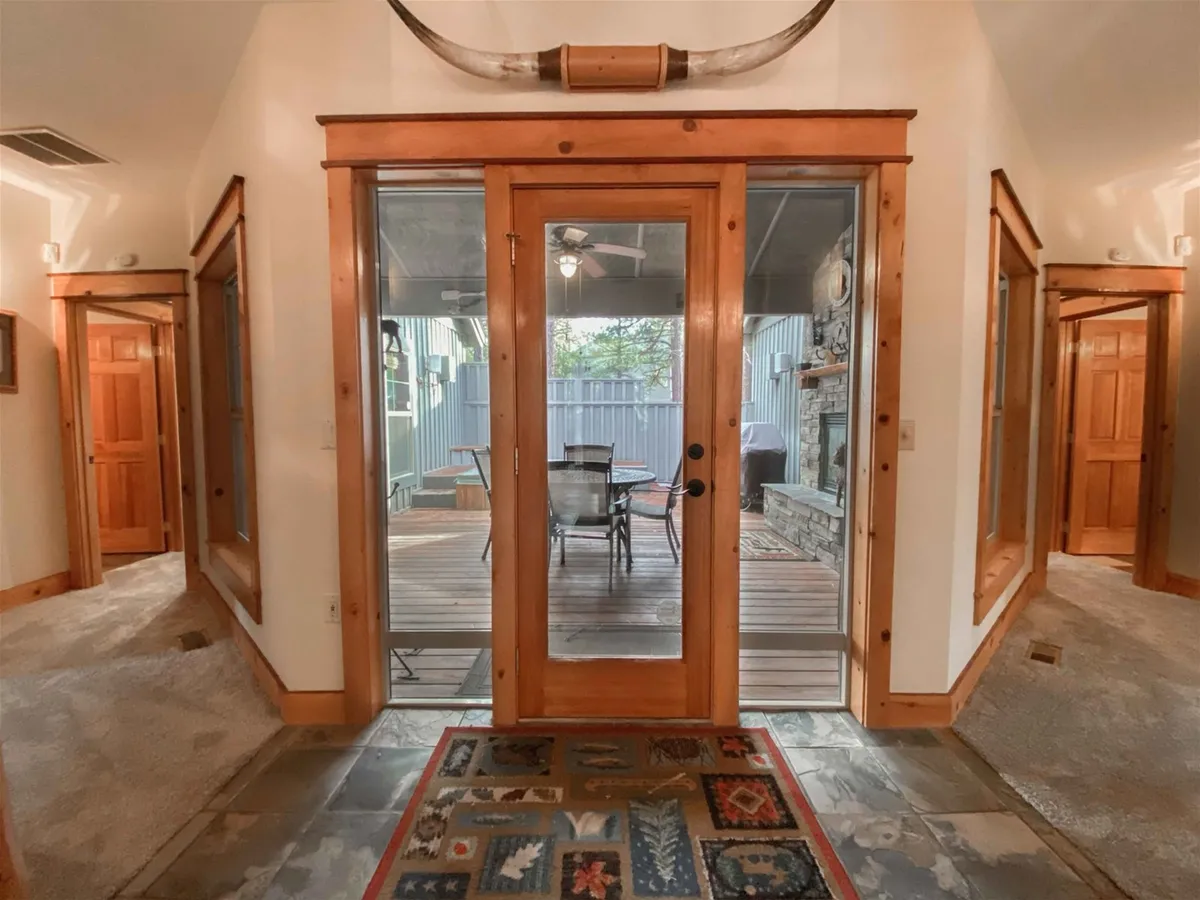 A rustic, inviting foyer with double glass doors leading outside, accented by wooden finishes and horn decor. The setting offers a transitional view from the cozy interior toward the covered porch, hinting at sunset views and the opportunity to step out to the deck for fireside relaxation or hot tub soaks.