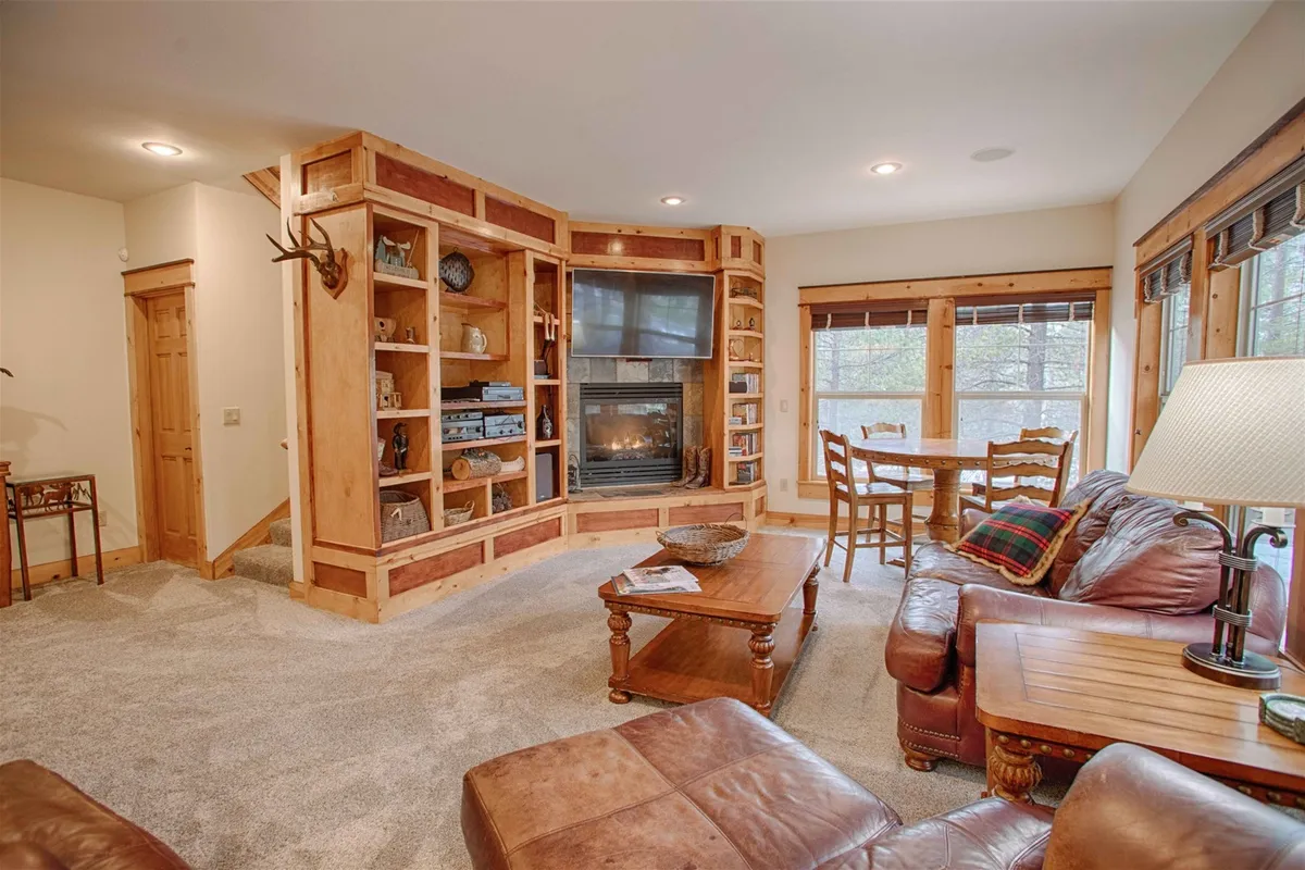 This image captures a spacious open-concept living and dining area, featuring a plush leather couch oriented toward a glowing gas fireplace. The room is accented with built-in bookshelves and a large wooden dining table, all bathed in soft, natural light streaming through the windows. The cozy yet grand environment is ideal for both casual relaxation and family gatherings.